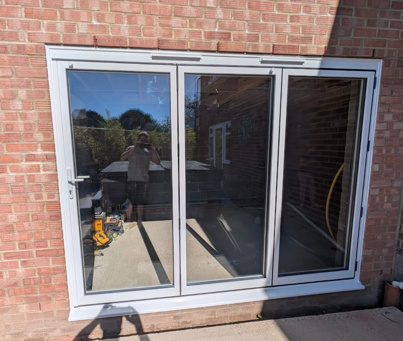 White three-pane bi-fold doors in a brick opening — by A1 Window Construction Ltd